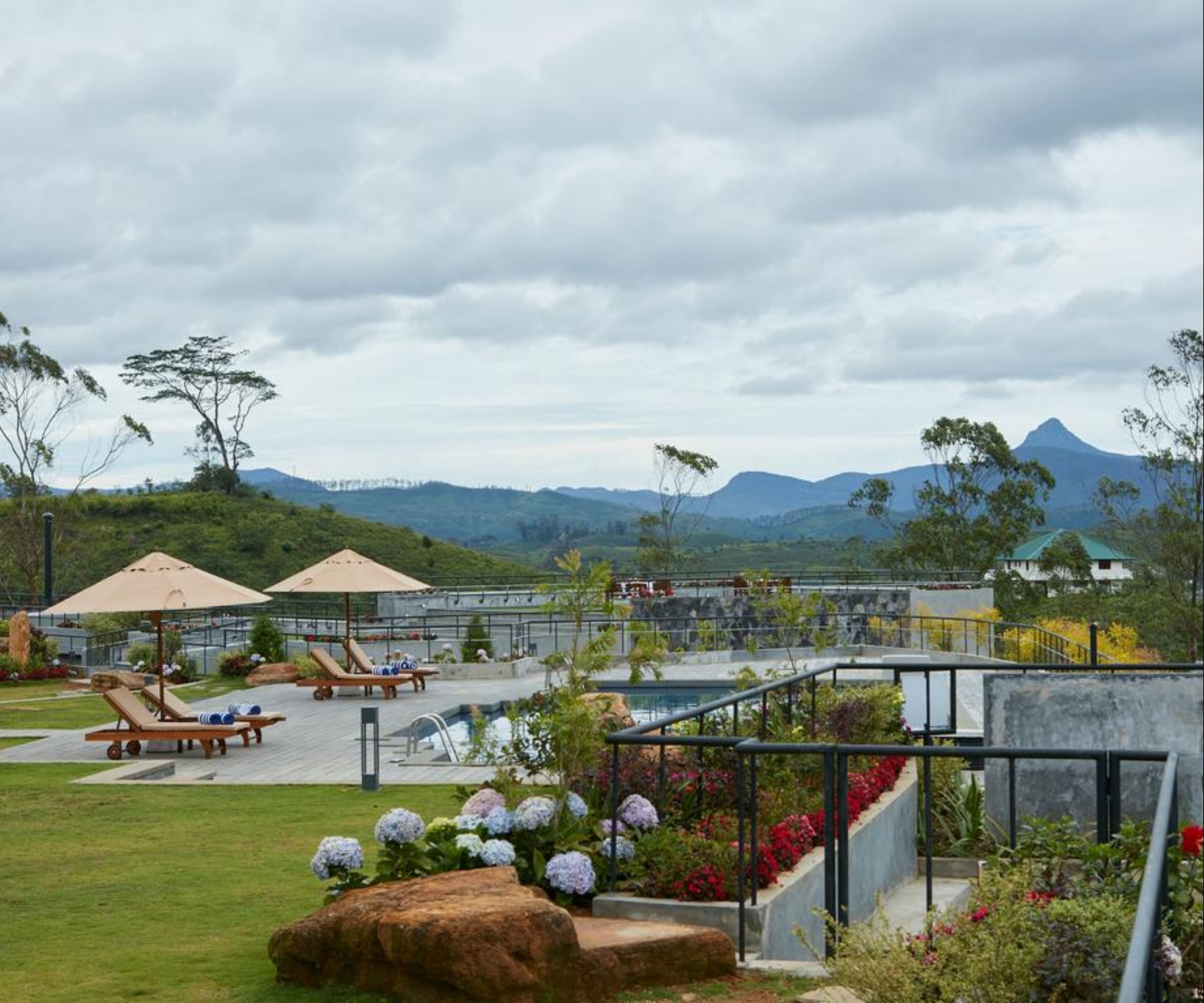 A pool area with lounge chairs and umbrellas, surrounded by landscaped gardens and a view of mountains.