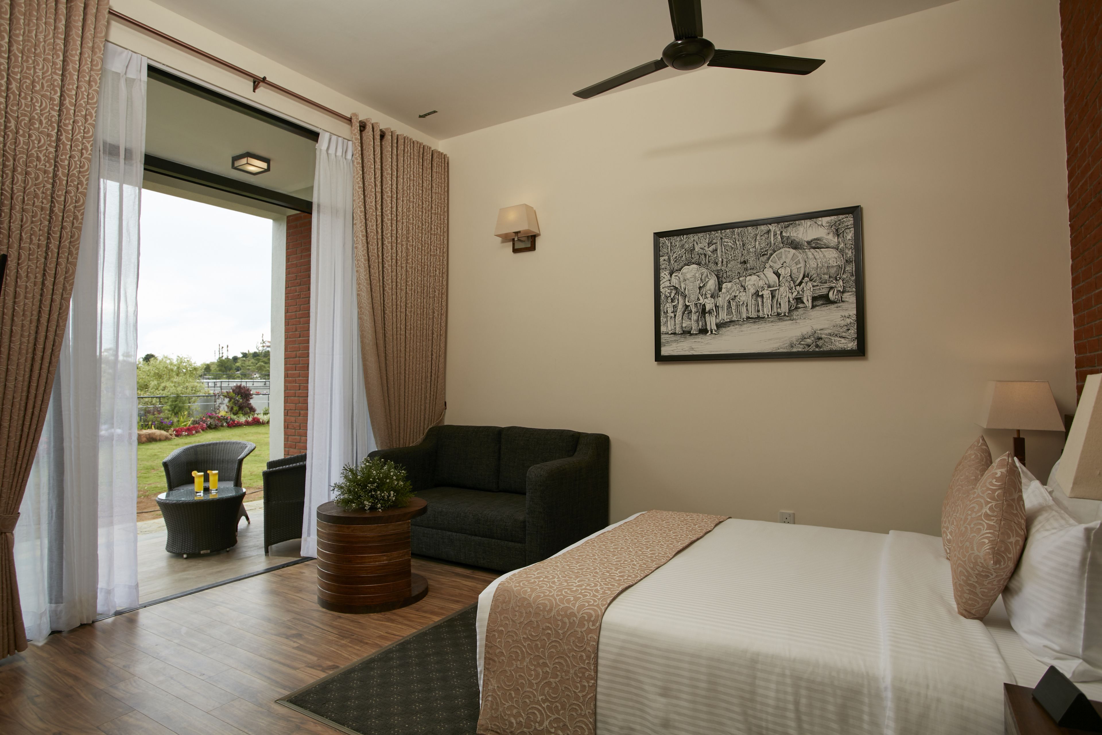 A hotel room with a bed, a sofa, a small table, a potted plant, and a picture on the wall.