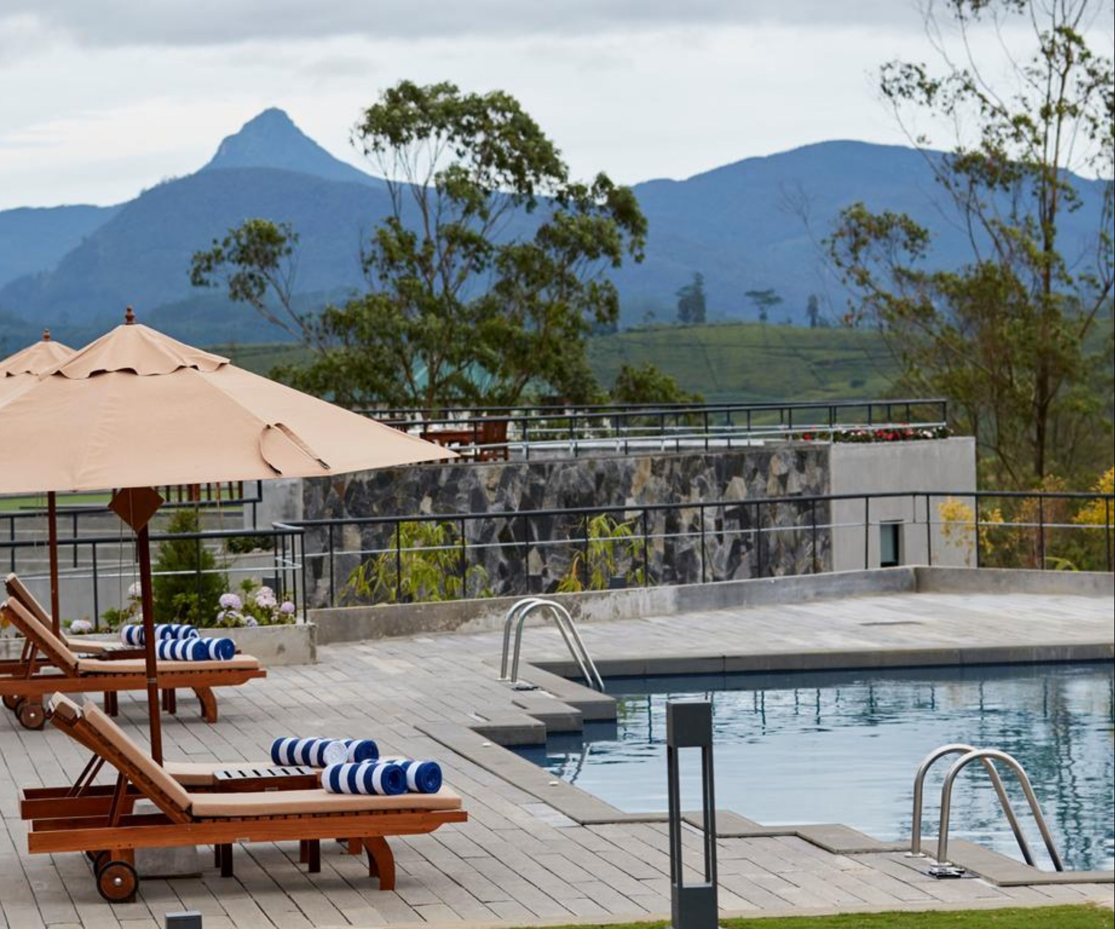 A poolside area with lounge chairs, a pool, and a view of mountains.