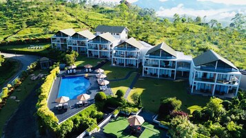 Un moderno resort con varias construcciones, una piscina central y abundante vegetación alrededor de la propiedad.