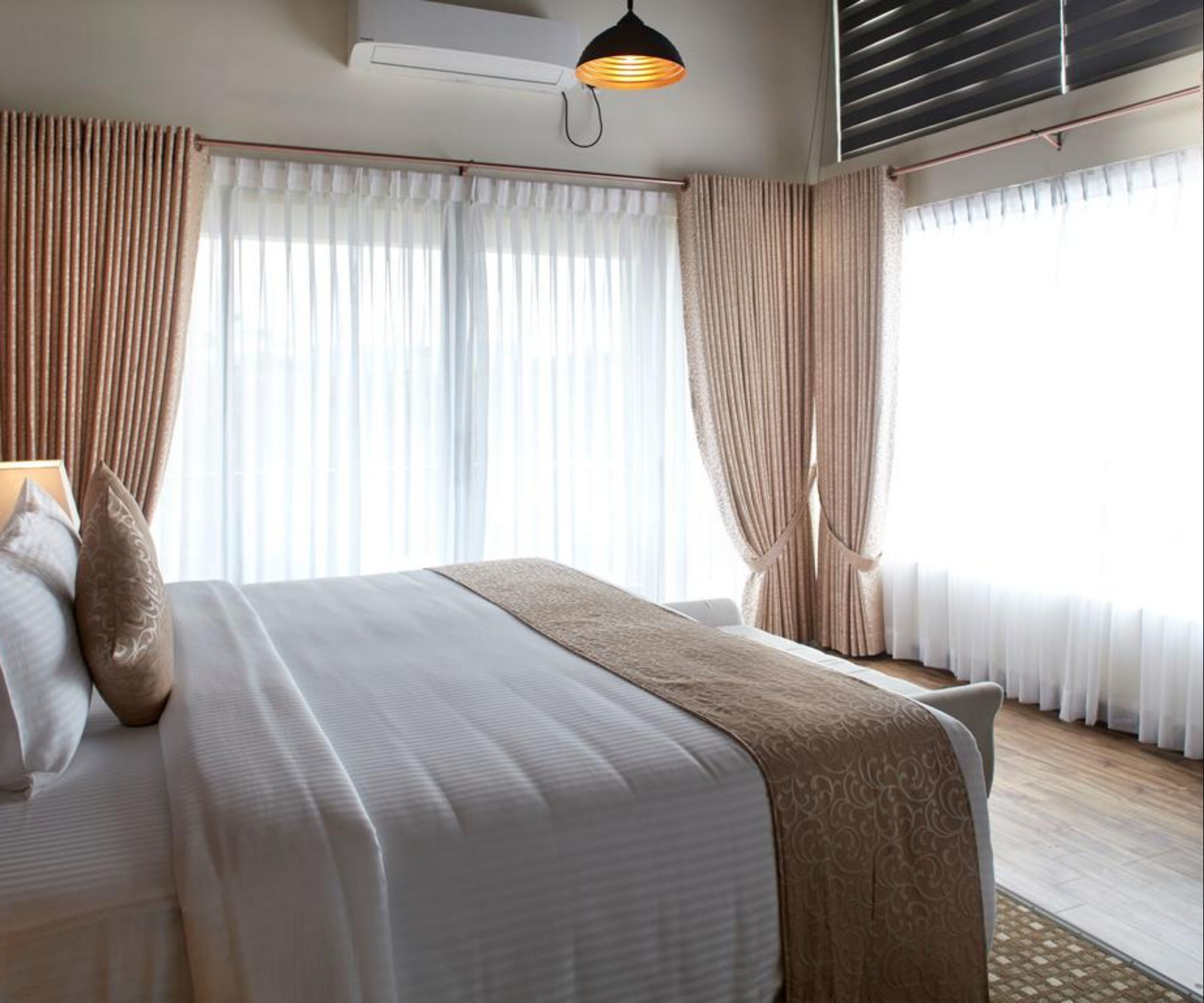 Habitación de hotel con una cama grande, cortinas color beige, una lámpara colgante y un equipo de aire acondicionado.