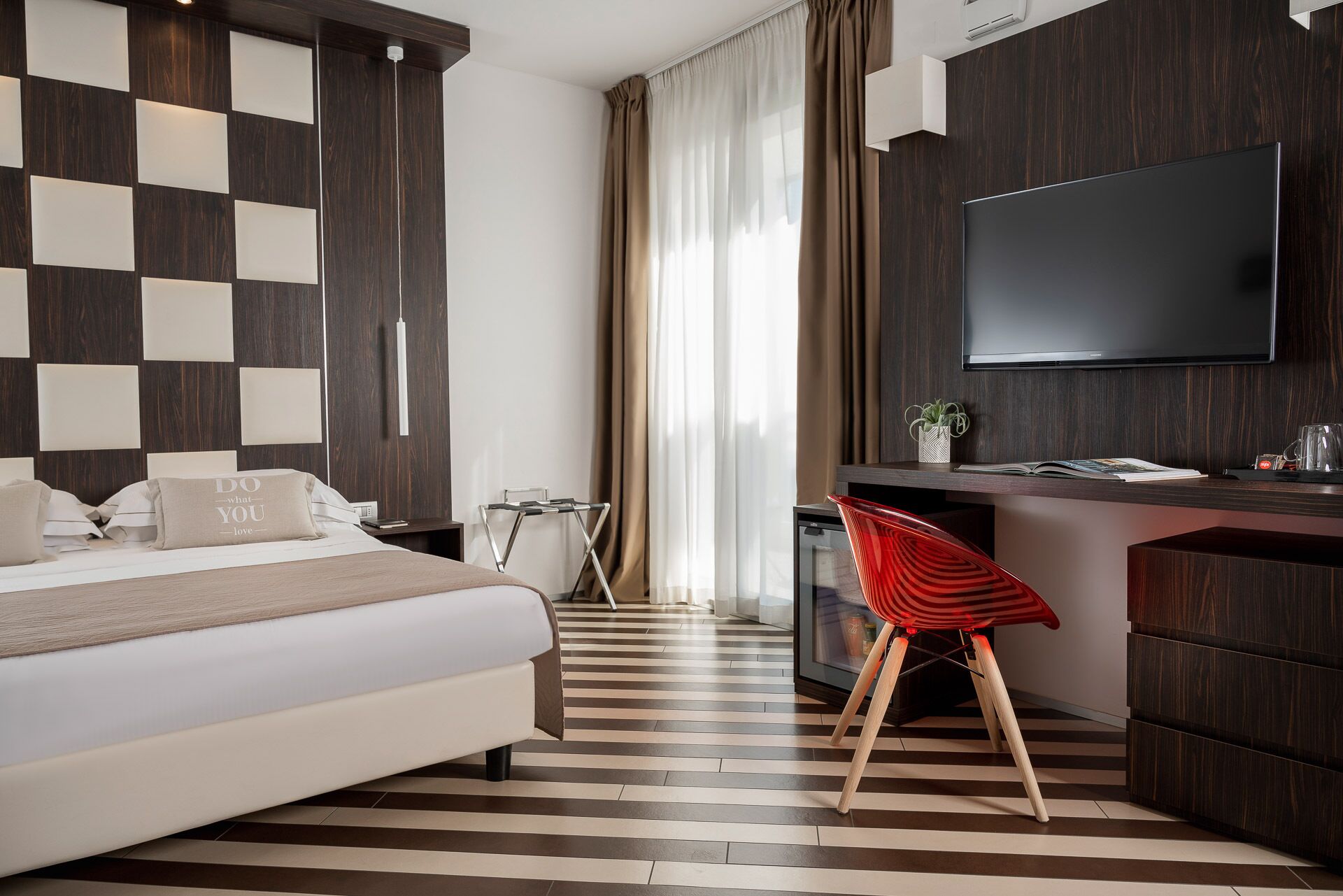 Una habitación de hotel moderna con una cama grande, un escritorio, un televisor y un suelo a rayas.