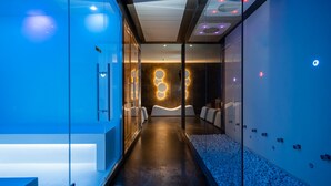 Un pasillo moderno y bien iluminado con paredes de vidrio, una zona de estar central y una lámpara de pared circular única.