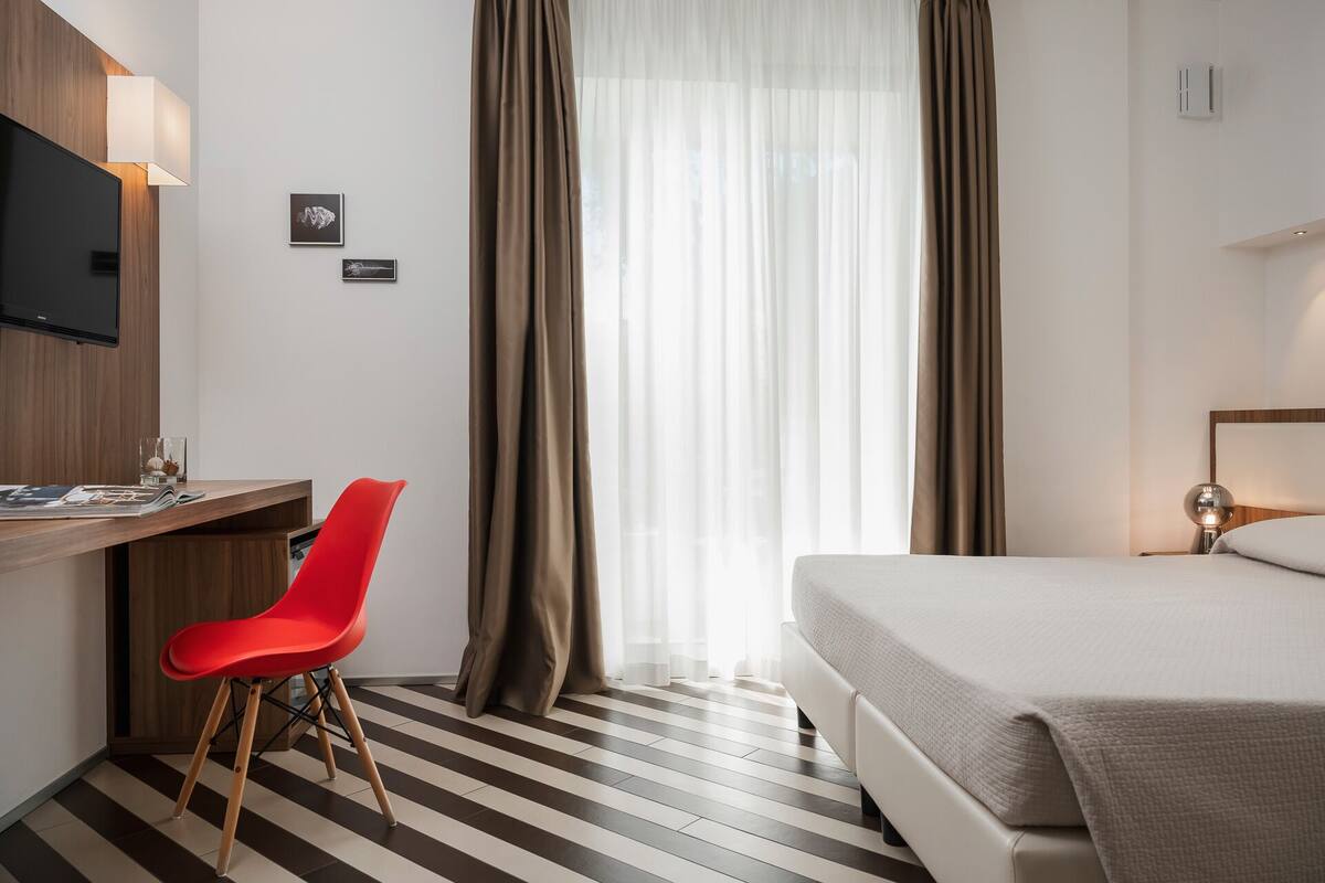 Een hotelkamer met een bed, een bureau met stoel, een televisie en gordijnen.