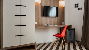 Una habitación moderna con un escritorio de madera, una silla roja, un televisor montado en la pared y un mueble pequeño.