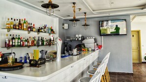 A bar area with shelves of liquor bottles, a coffee machine, and a television mounted on the wall. - SunRose Beach Aparthotel (Corfu)