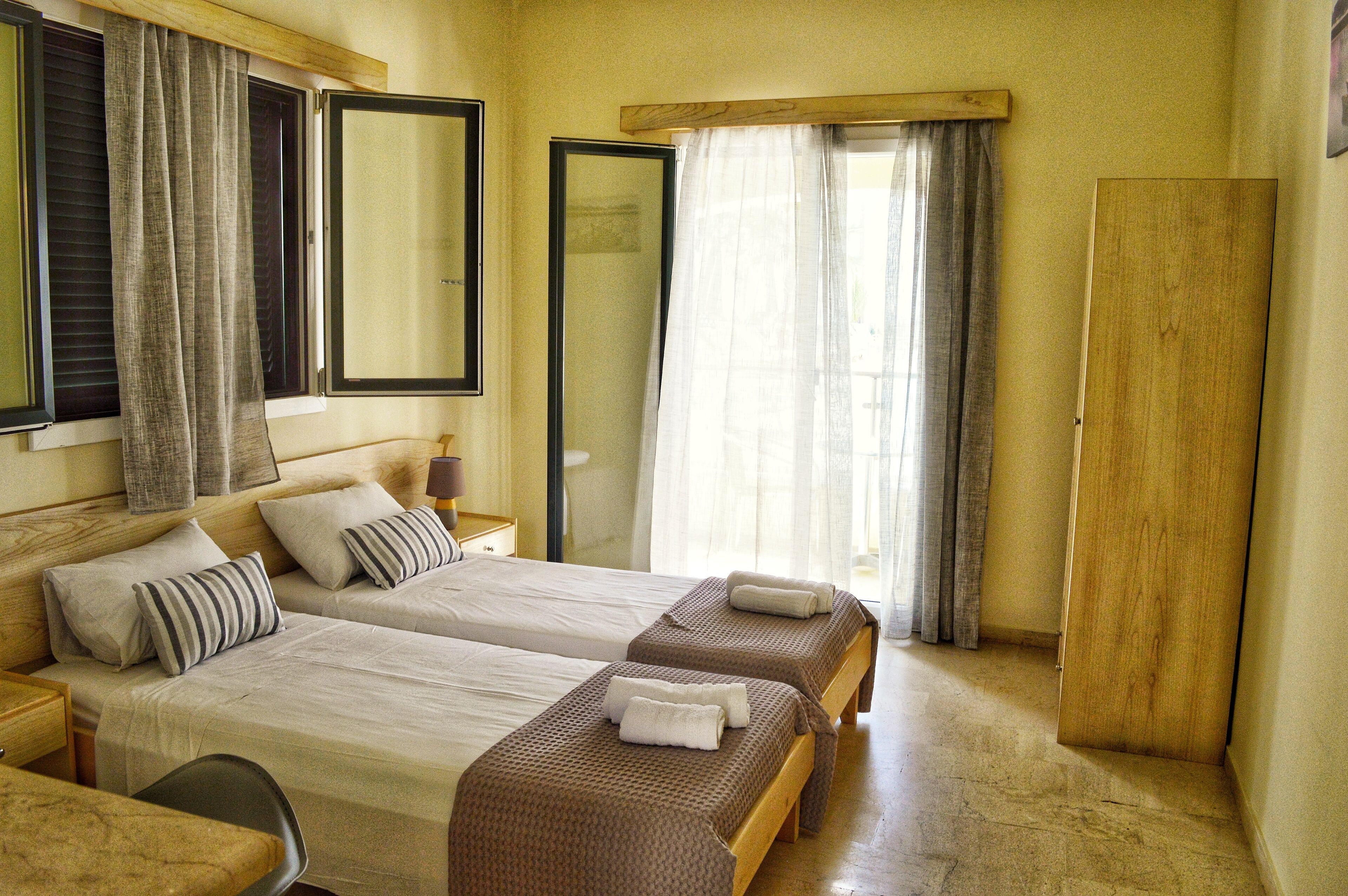 A hotel room with two beds, a wooden wardrobe, a desk, and a chair.