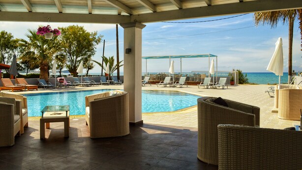 A poolside area with lounge chairs, a small table, and a covered seating area overlooking the sea. - SunRose Beach Aparthotel (Corfu)
