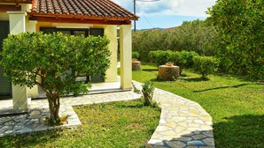 A house with a tiled roof, a stone pathway, and a well-maintained garden with various shrubs and a small tree. - SunRose Beach Aparthotel (Corfu)
