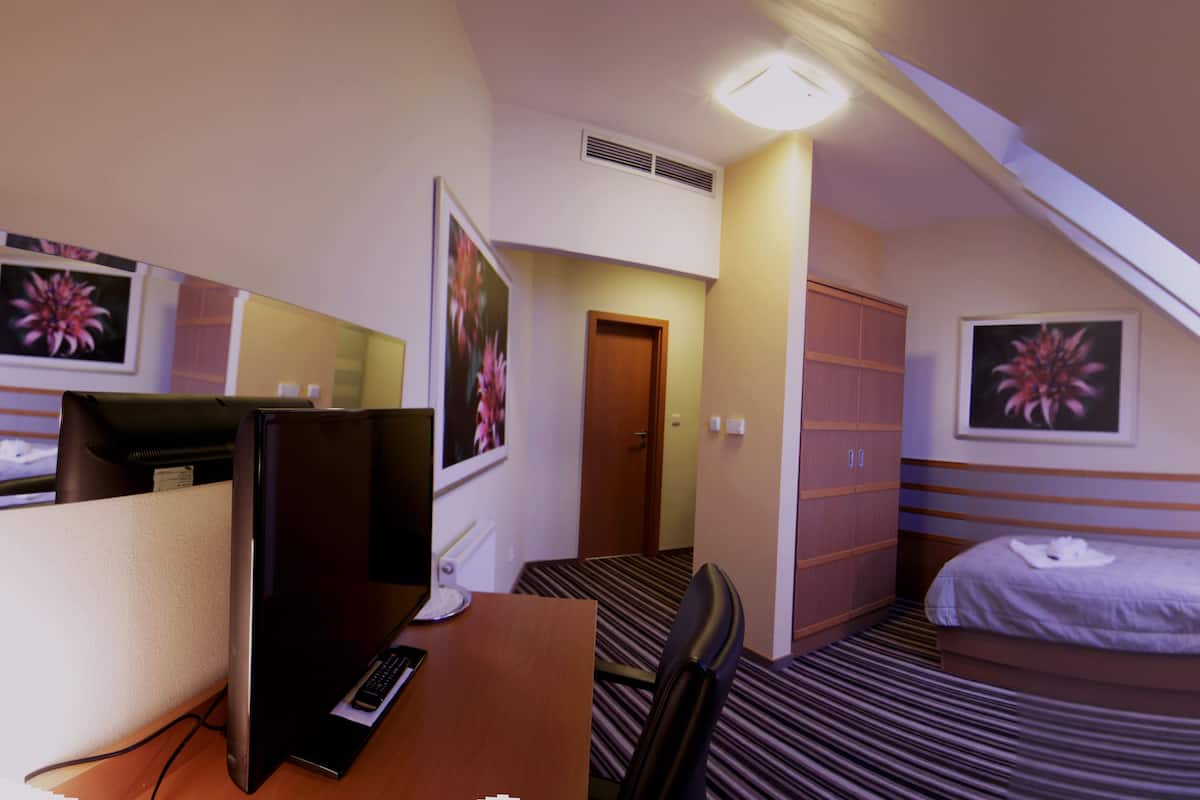 A hotel room with a desk, a bed, a TV, a door, and a window.