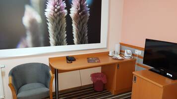 A hotel room with a desk, chair, television, and a large window with a floral view.