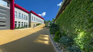 Un edificio moderno con facciata rosso e grigio, un vialetto lastricato e una parete verde con piante rampicanti.