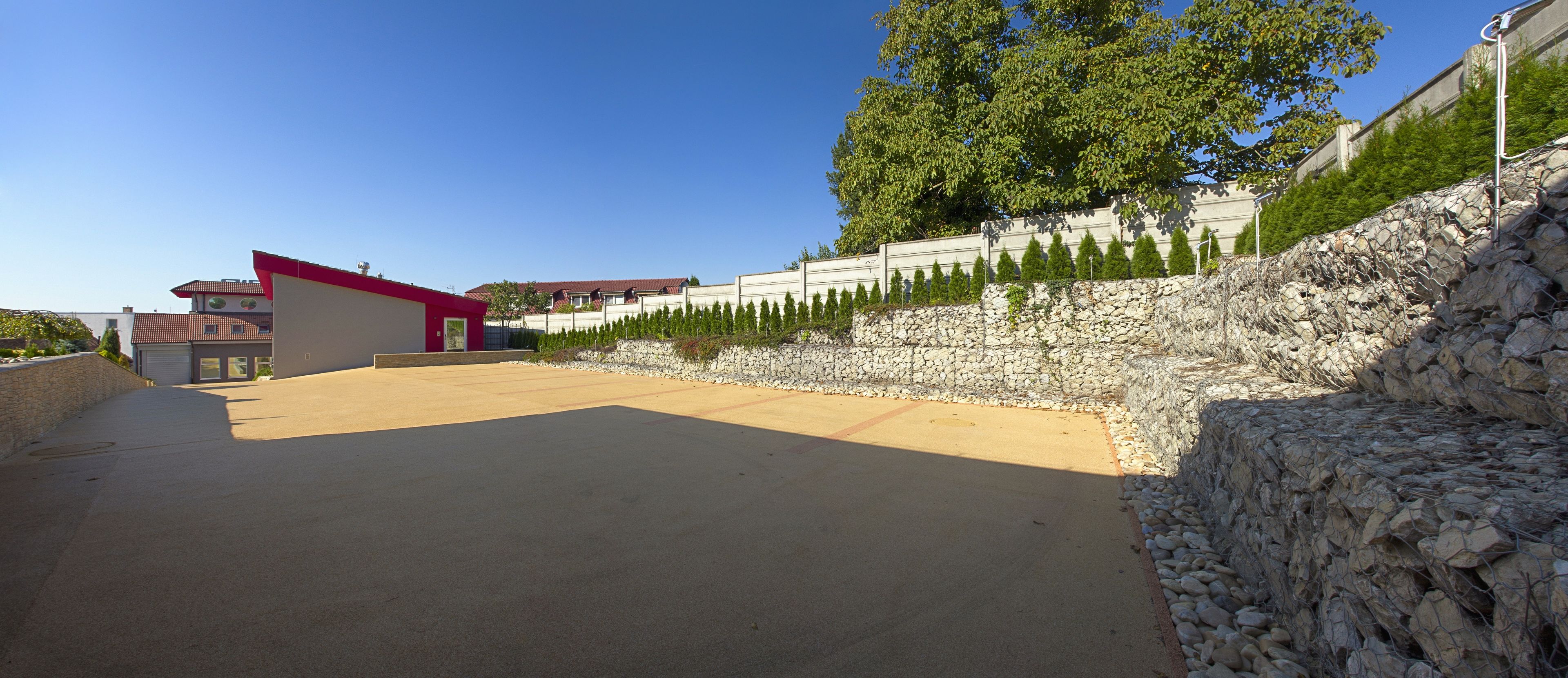 Un espace de stationnement doté d’une surface pavée, d’un mur de soutènement en pierre et d’un bâtiment avec un toit rouge.
