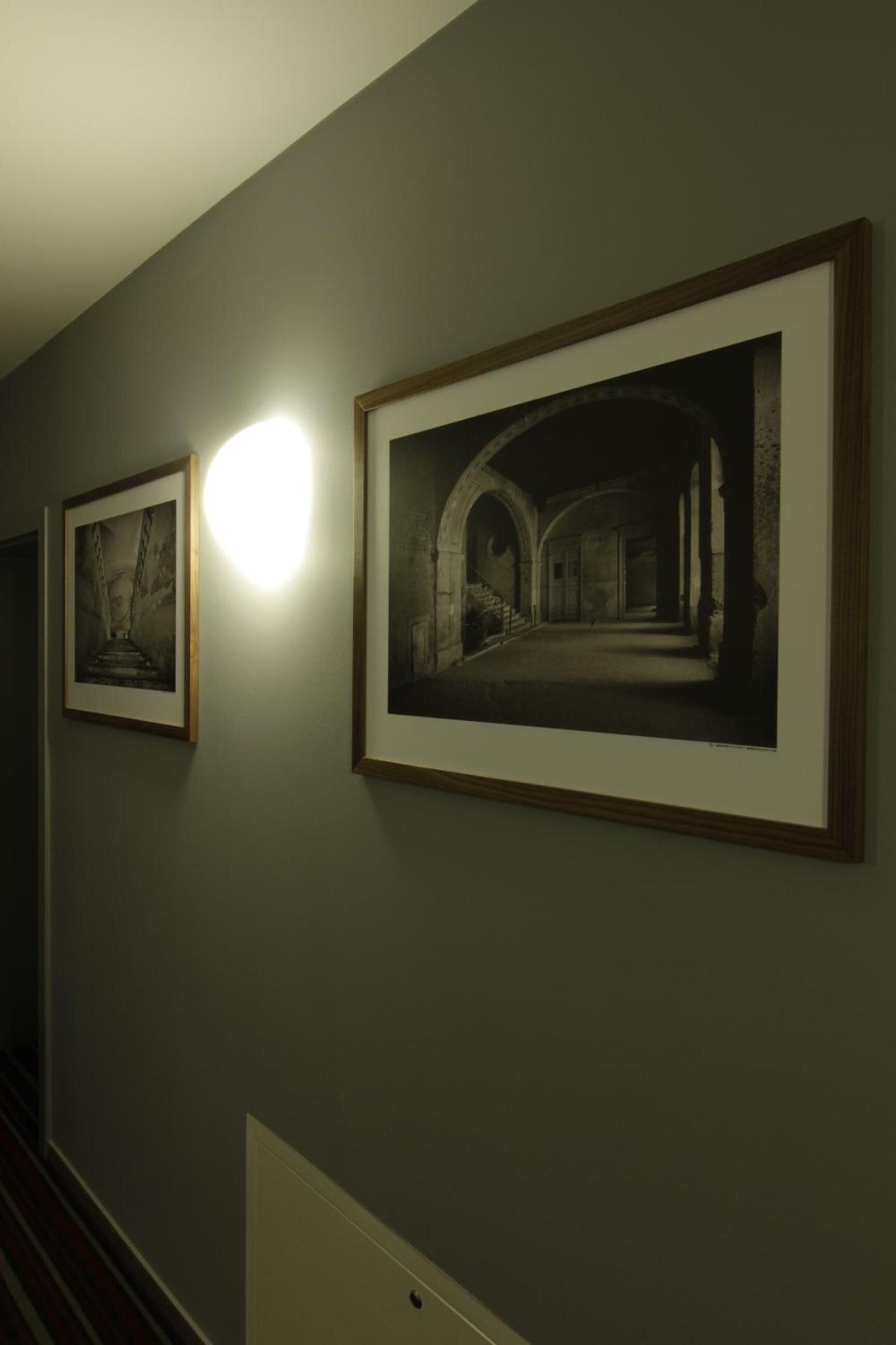 A hallway with framed photographs on the wall and a light fixture above them.