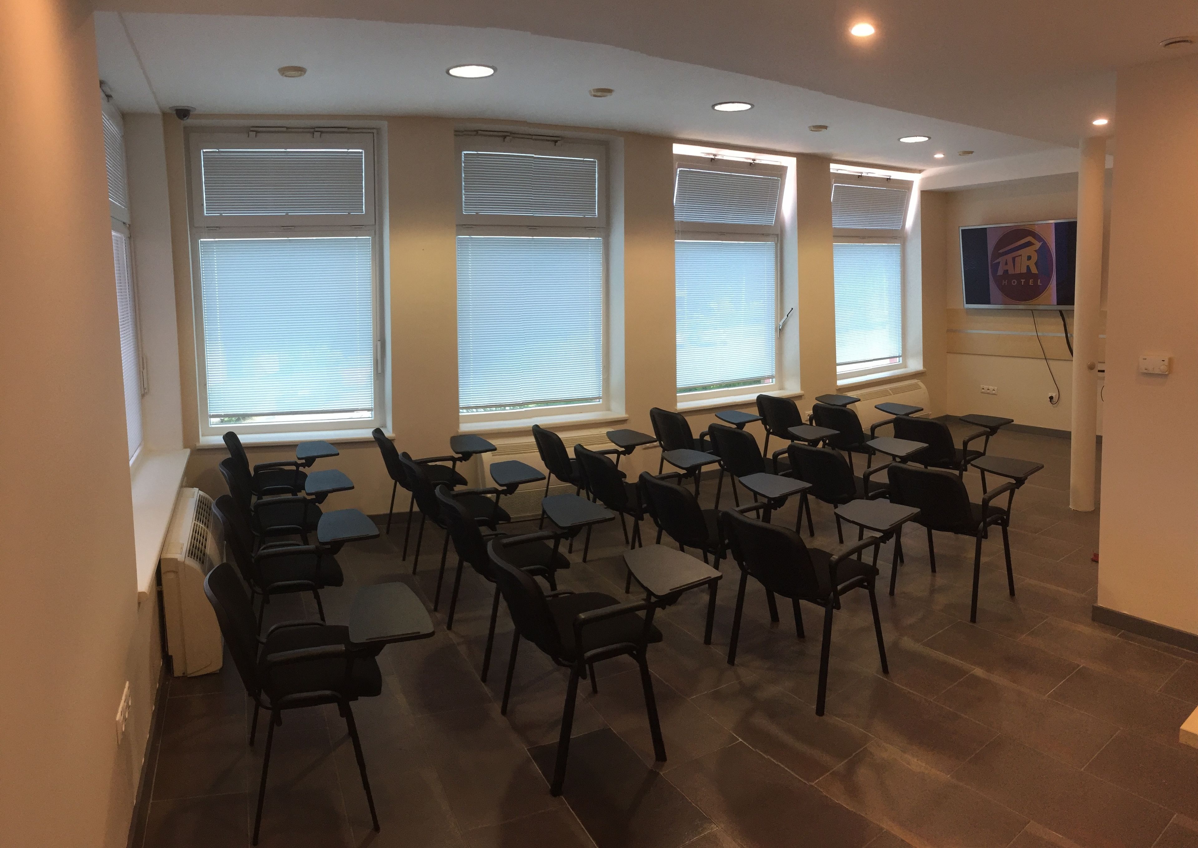 A conference room with rows of chairs and tables, large windows with blinds, and a ceiling with recessed lighting.