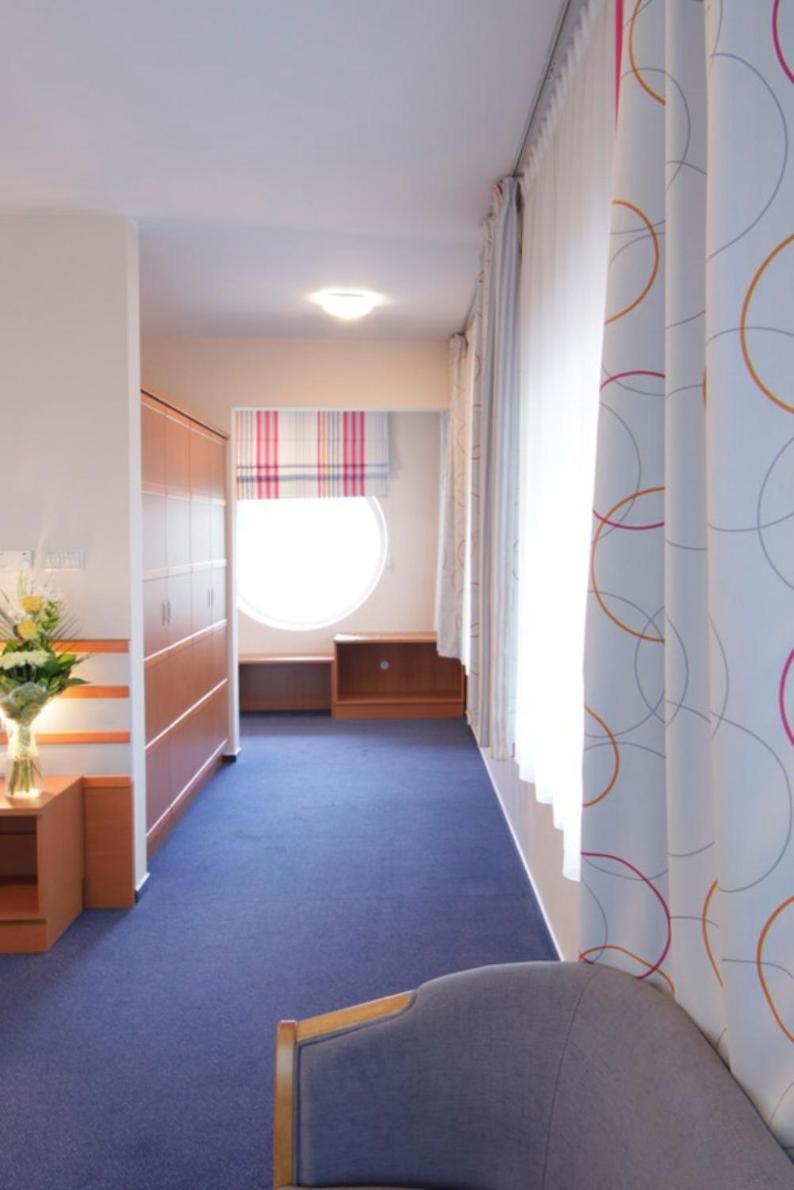 A hotel room with a bed, a desk, a chair, a wardrobe, and a window with curtains.