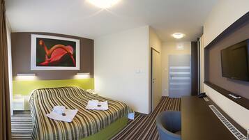 Une chambre d’hôtel avec un lit, une télévision, un tableau et un bureau avec une chaise.