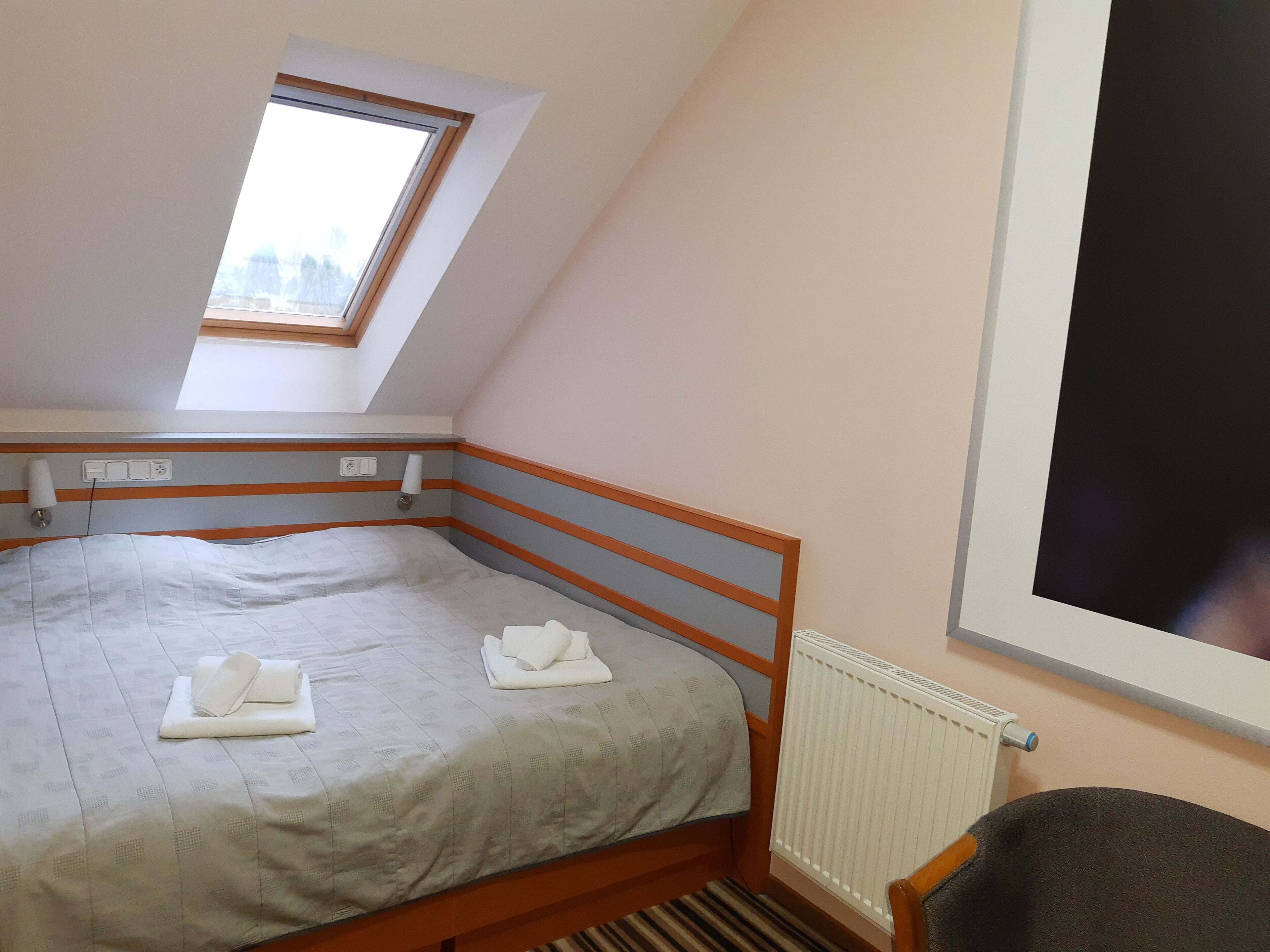 A bedroom with a single bed, a window, a radiator, and a power outlet on the wall.