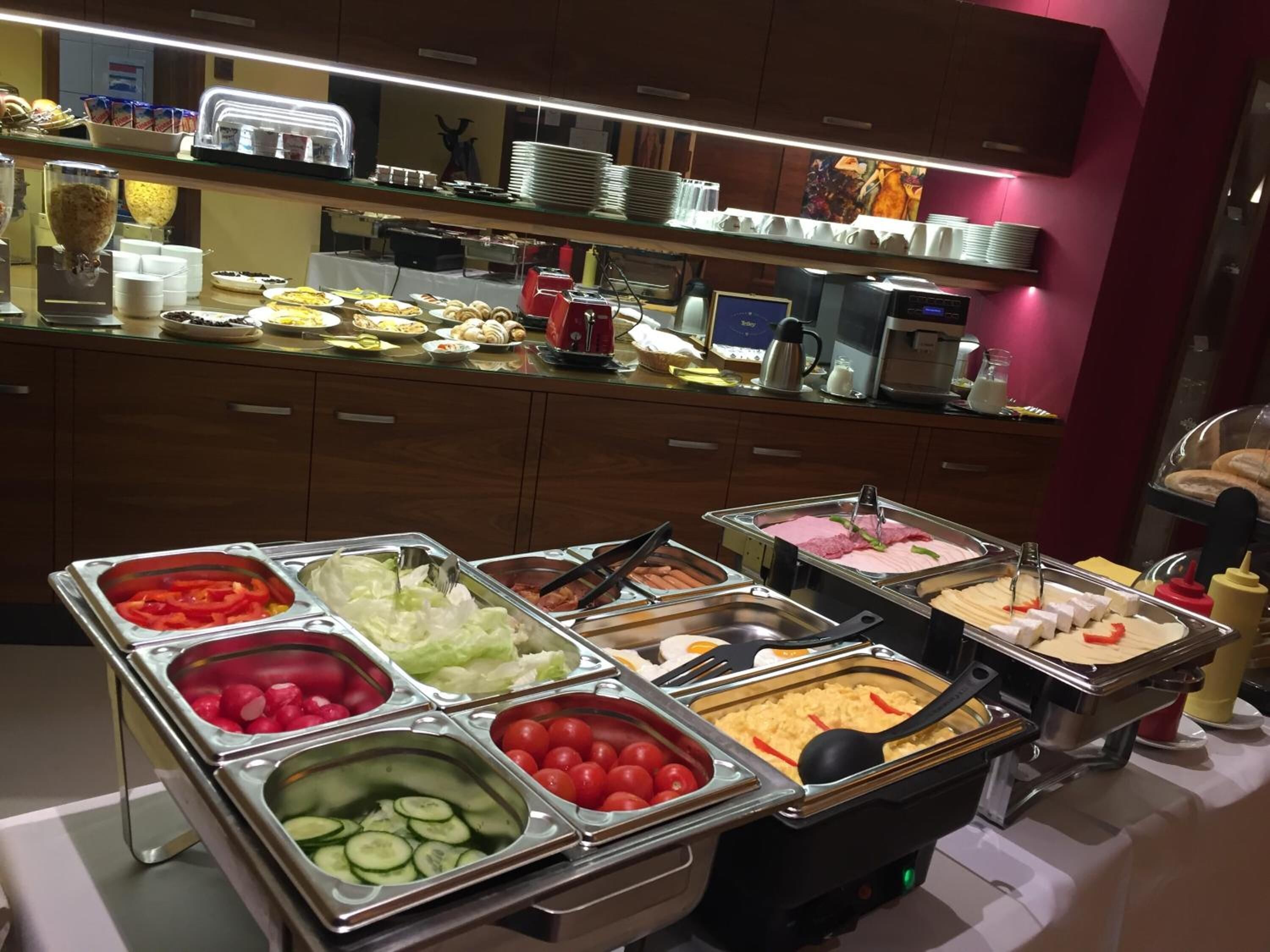 A buffet with various food items including fruits, vegetables, and hot dogs.