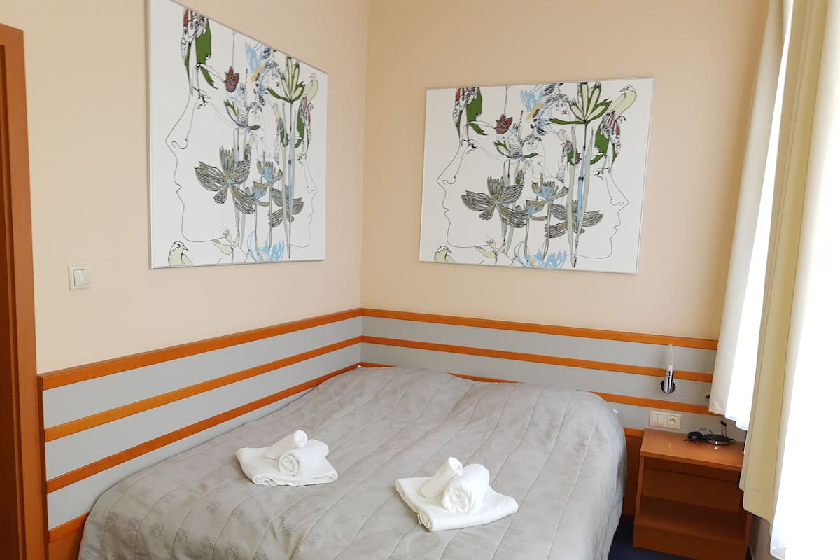 A bedroom with a bed, two towels, a nightstand, a lamp, and two floral artwork pieces on the wall.