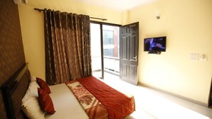 Quarto com cama, cortinas, televisão e porta de correr para área externa.
