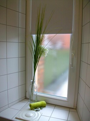 Une salle de bain avec une fenêtre, un vase contenant des plantes vertes, une serviette jaune et un porte-savon blanc.