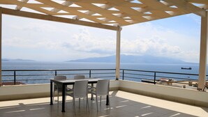 Una terraza al aire libre con una mesa y sillas, con vistas a una masa de agua y montañas distantes.