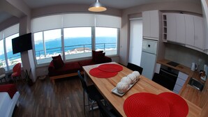 Una cocina moderna con mostrador de madera, una mesa de comedor con individuales rojos y vista al océano a través de amplios ventanales.