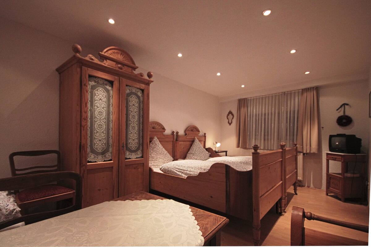 Une chambre à coucher avec un lit en bois, une armoire en bois, une table de chevet et un téléviseur posé sur un meuble.