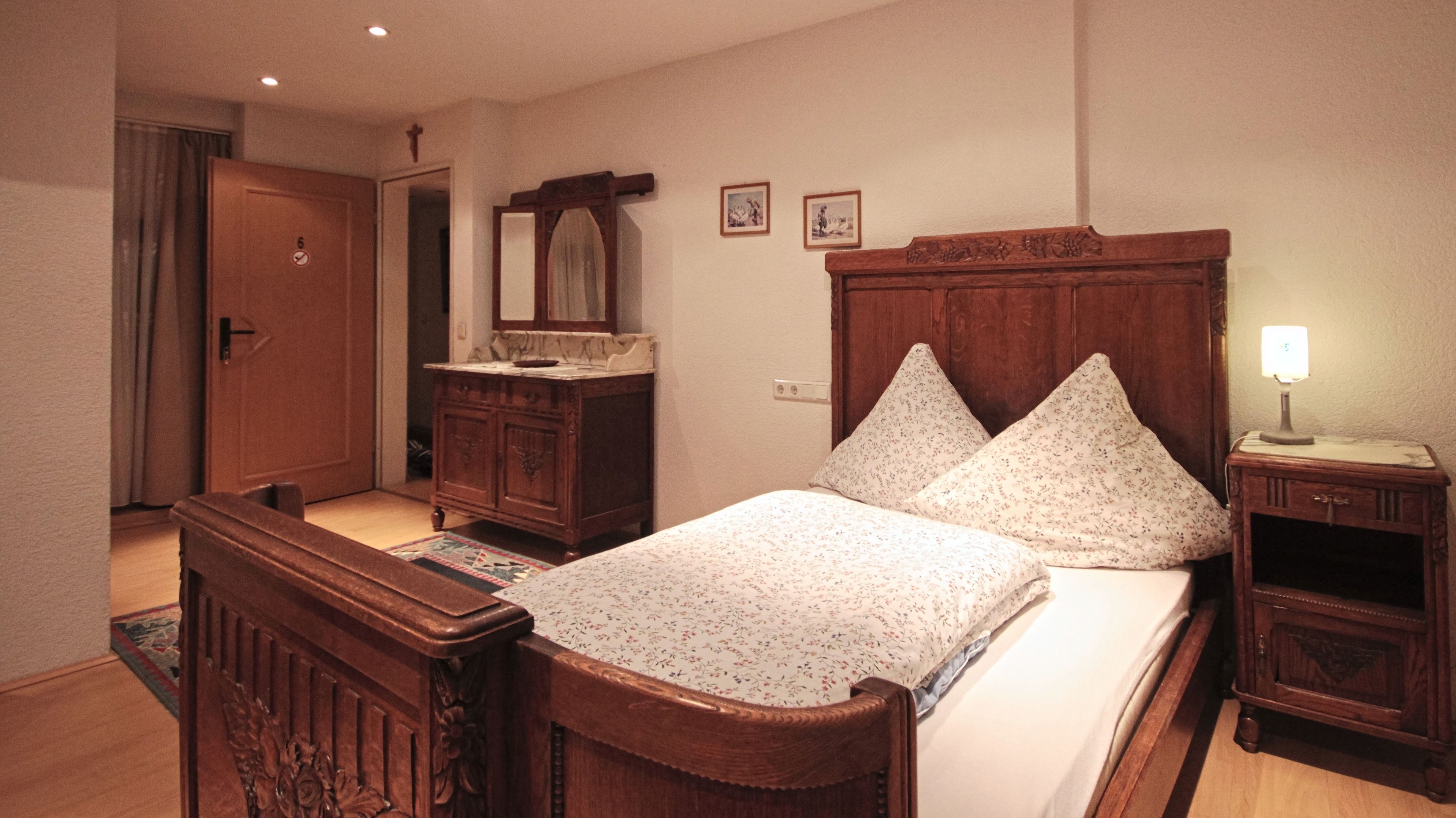 A bedroom with a wooden bed, a nightstand with a lamp, a dresser, a mirror, and two framed pictures on the wall.