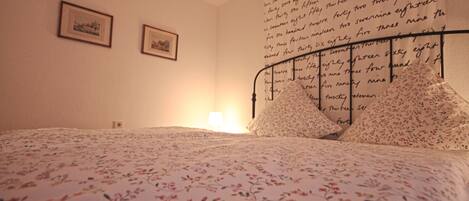 A bedroom with a floral bedspread, a metal bed frame, and two framed pictures on the wall.
