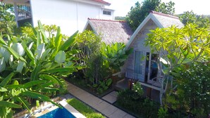 Et hus med rødt tegltag, omgivet af frodig vegetation og en swimmingpool.