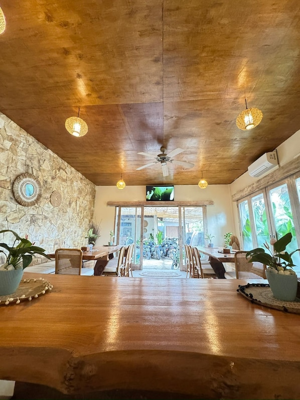 A spacious dining area with a wooden table, stone wall, and ceiling fan. - Lavella Villa's (Kuta)