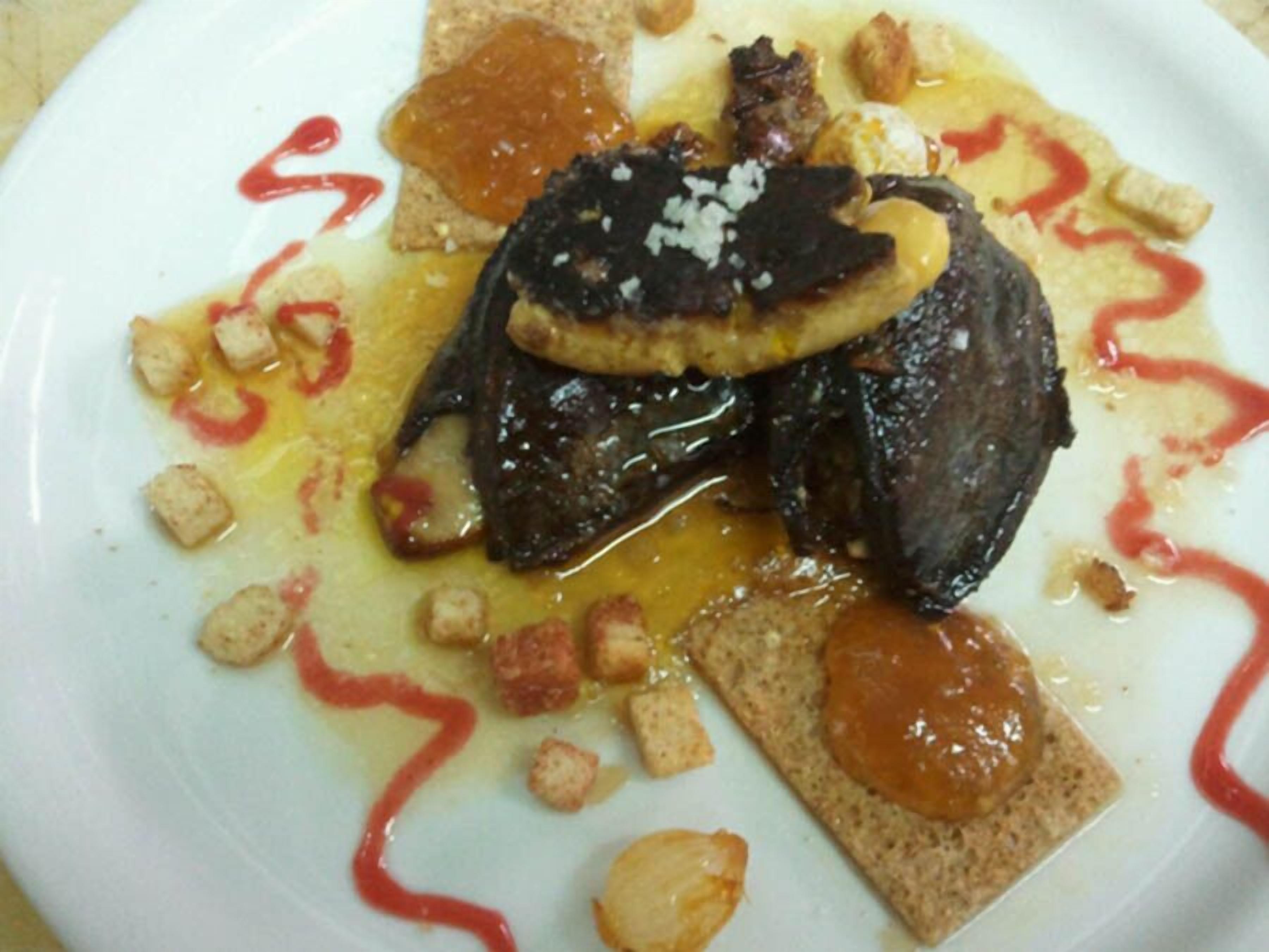 A plate with a meat dish, possibly steak, topped with a dark sauce and garnished with croutons and a slice of cheese.