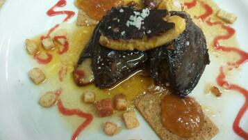 A plate with a meat dish, possibly steak, topped with a dark sauce and garnished with croutons and a slice of cheese.