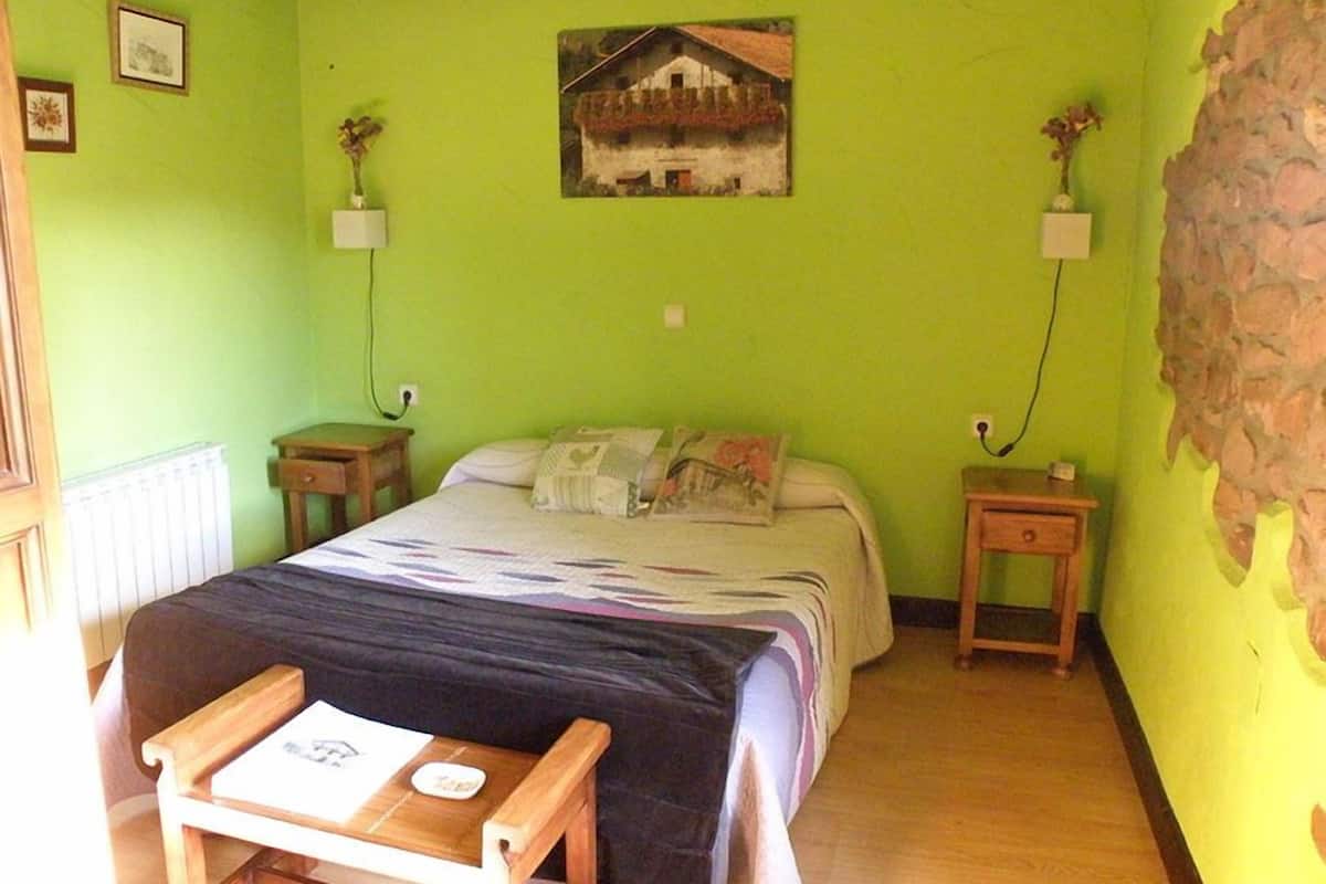 A room with a bed, a small wooden table, and a wall-mounted picture.