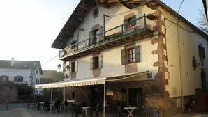 A two-story building with a balcony, outdoor seating area, and stone facade. - Posada Elbete (Baztan)