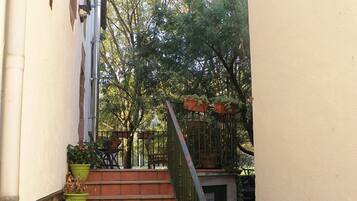 Una escalera exterior estrecha que conduce a una zona cubierta con plantas en macetas y barandilla de metal.