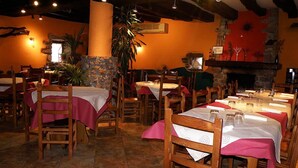 A restaurant with wooden tables and chairs, stone walls, and a fireplace. - Posada Elbete (Baztan)