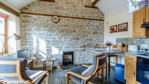A cozy room with a stone wall, a fireplace, wooden furniture, and a kitchen area. - Highgrove Barns (Craven Arms)