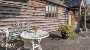 A rustic log cabin with a wooden door, a window, and a small porch area. - Highgrove Barns (Craven Arms)
