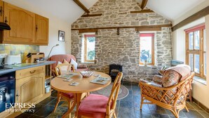 A cozy kitchen with wooden cabinets, a stone wall, and a dining area with wicker furniture. - Highgrove Barns (Craven Arms)