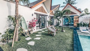 Una casa moderna con piscina, césped y algunas palmeras.