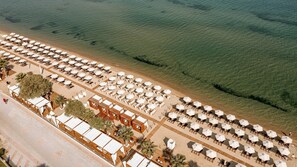 An aerial view of a beach resort with rows of sun loungers and umbrellas, a wooden deck area, and a clear view of the ocean. - Wellness Santa Hotel - Adults Only (Thermaikos)