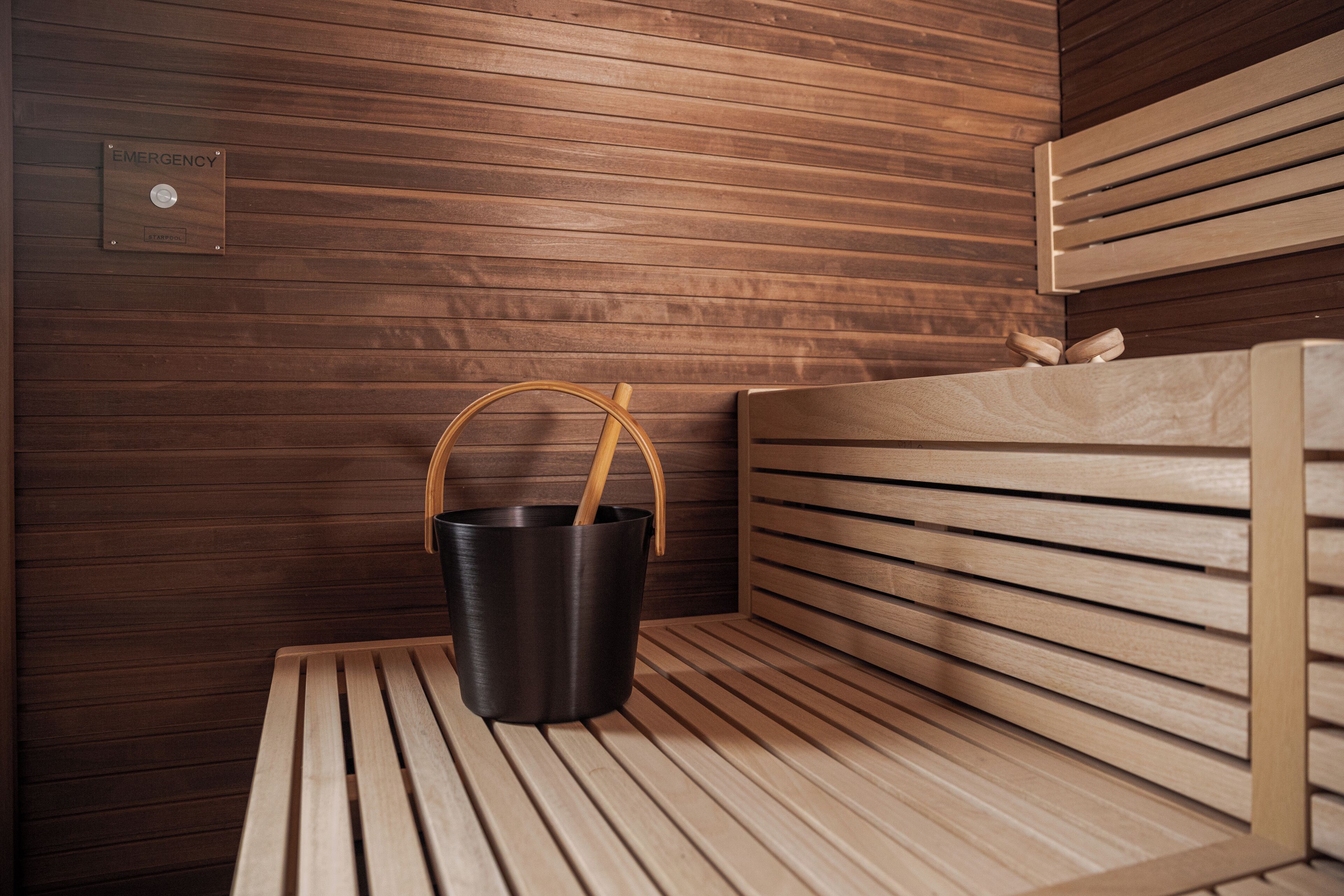 Un banco de madera con un cubo negro y asas de madera, un muro de madera con listones horizontales y un cartel de emergencia.