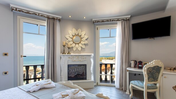Um quarto com cama, lareira, televisão e vista para o mar.