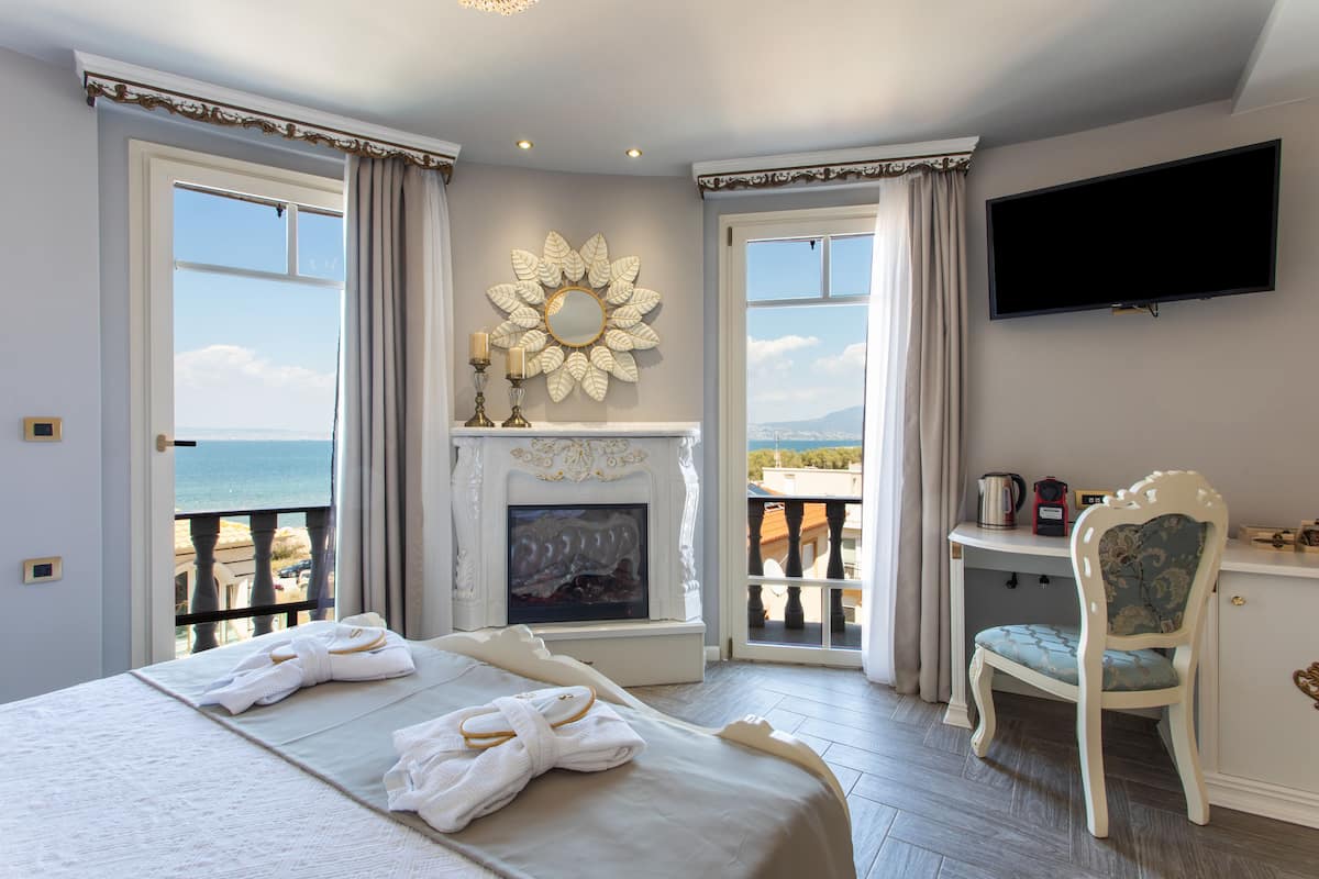 A bedroom with a bed, a fireplace, a television, and a view of the sea.