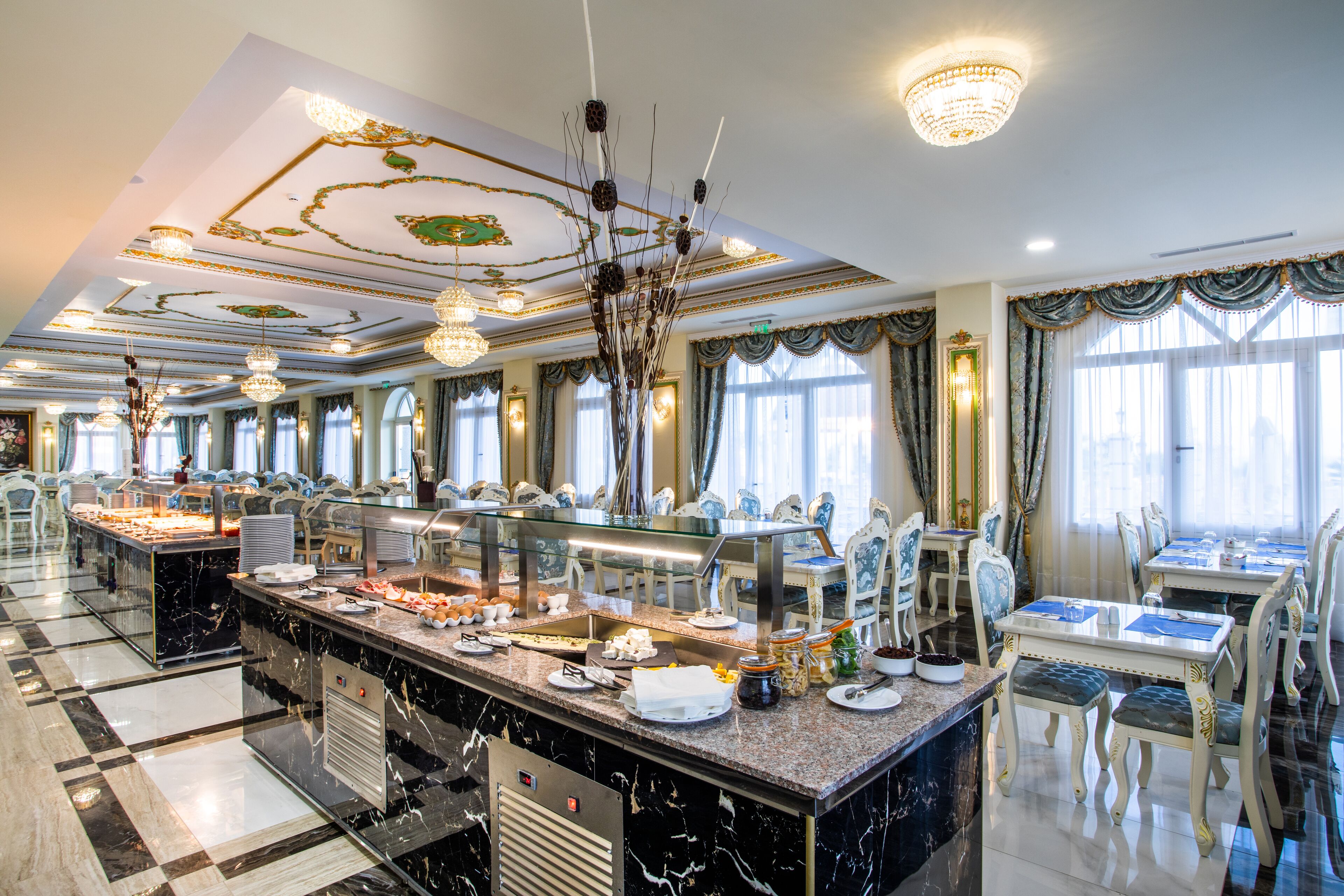 A spacious dining area with marble countertops, multiple dining tables, and elegant chandeliers.