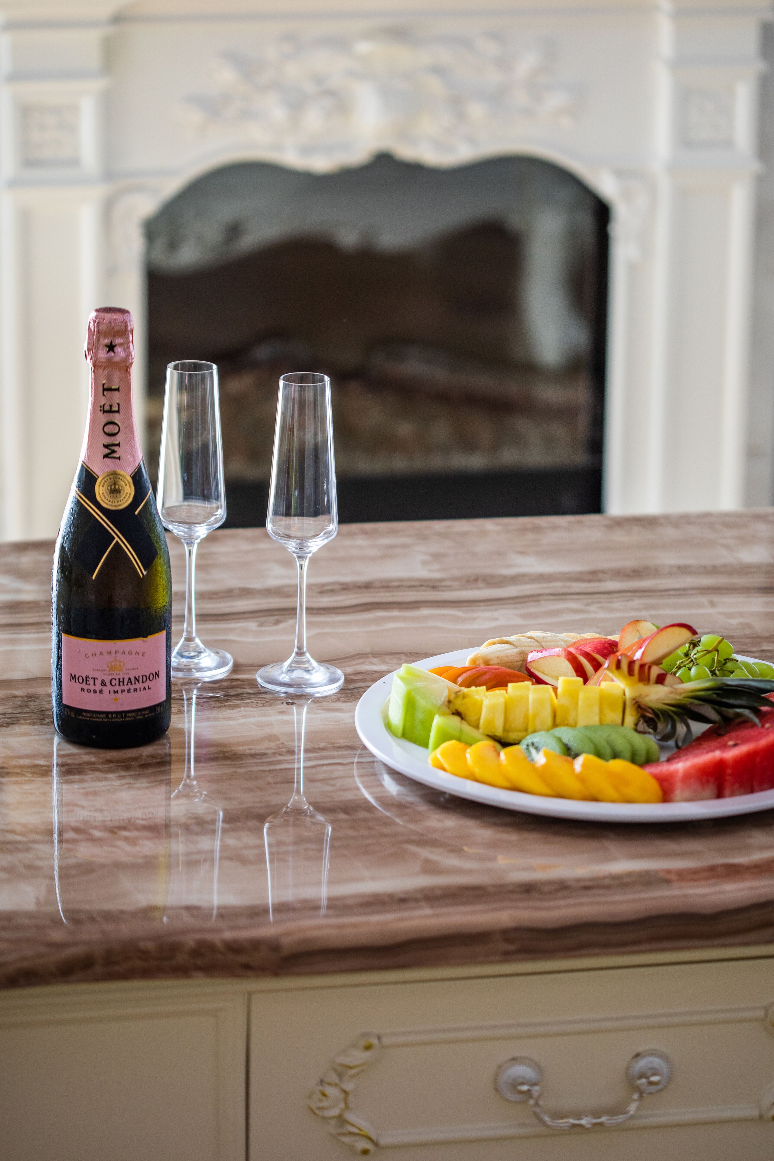 Eine Flasche Moët & Chandon Champagner, zwei leere Gläser und eine Fruchtschale auf einem Marmortisch.