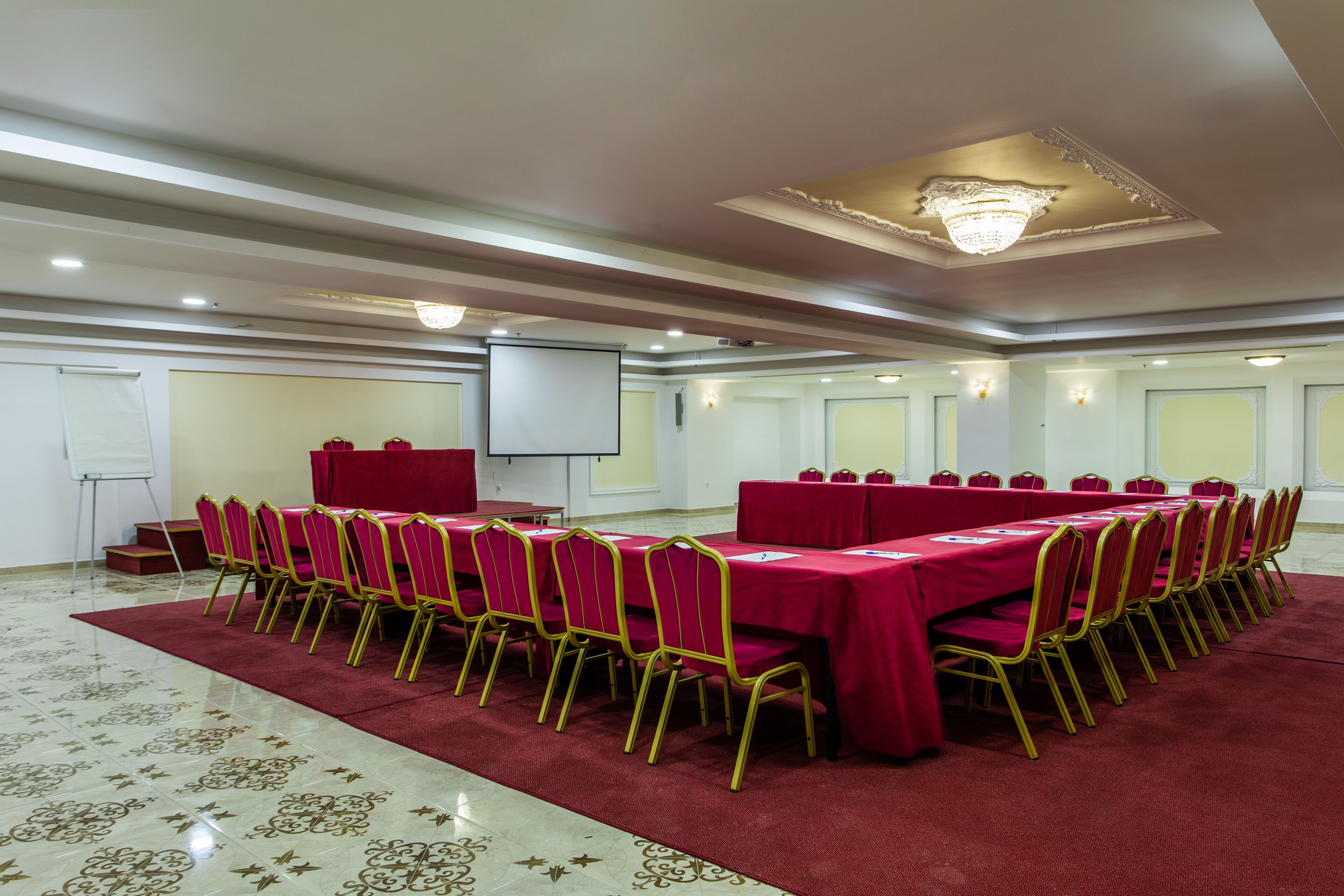A conference room with a long table, chairs, a projector screen, and a carpeted floor.